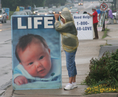 Alberta Rael holds a LIFE sign in the rain in Naperville, July 19
