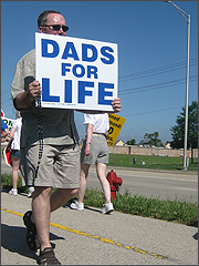A father carries a 'Dads for Life' sign while praying the Rosary at the June 20 protest.