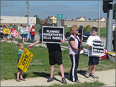 A family holds signs at the corner of New York Street and Oakhurst Drive.