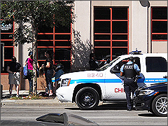 A second police officer consults with Officer Stevens (sitting in the car) while pro-lifers (left) pray outside of Planned Parenthood in Chicago.